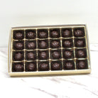 Box of 24 pieces of rounded dome shaped dark chocolates on a marble surface with a white background
